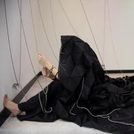 A woman holding onto various ropes, covered in a black draping structure 