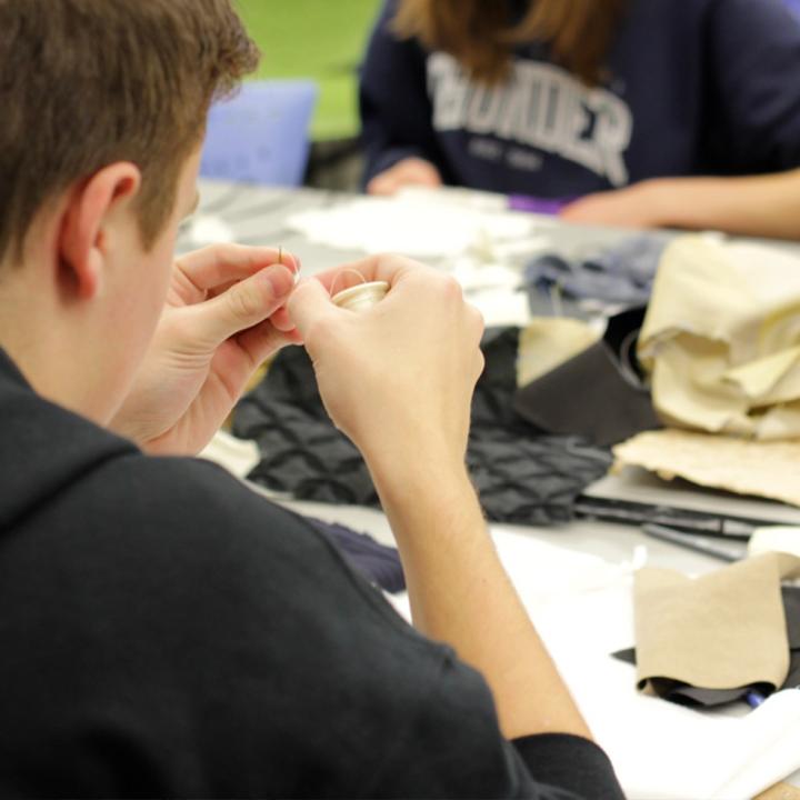 A student threads a needle. 