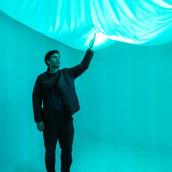 Person standing in a white gallery room touching a fabric panel that lights up